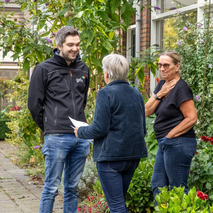 Twee oudere dames spreken in hun voortuin met een NOK.5-medewerker tijdens een opruimdag.