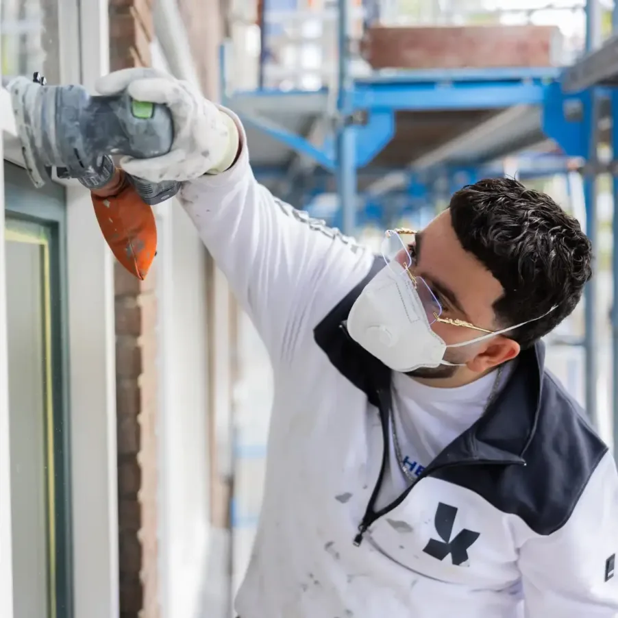 Man draagt beschermende handschoenen en mondkapje tijdens het schuren voor zijn veiligheid.