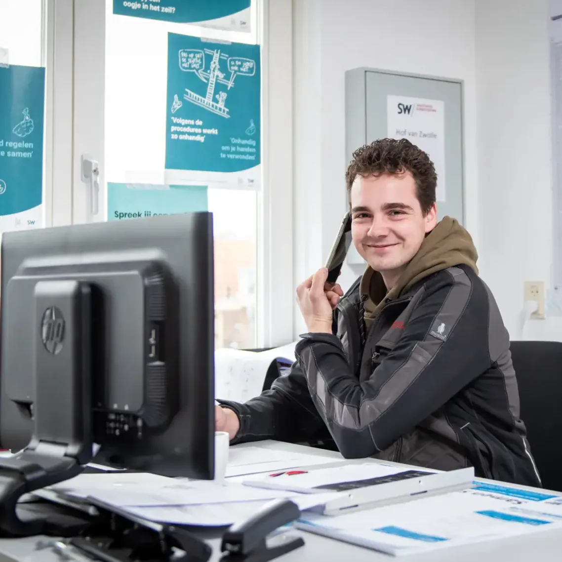 Medewerker aan een bureau met computerscherm en papieren laat zien hoe het is om te werken bij NOK.5.
